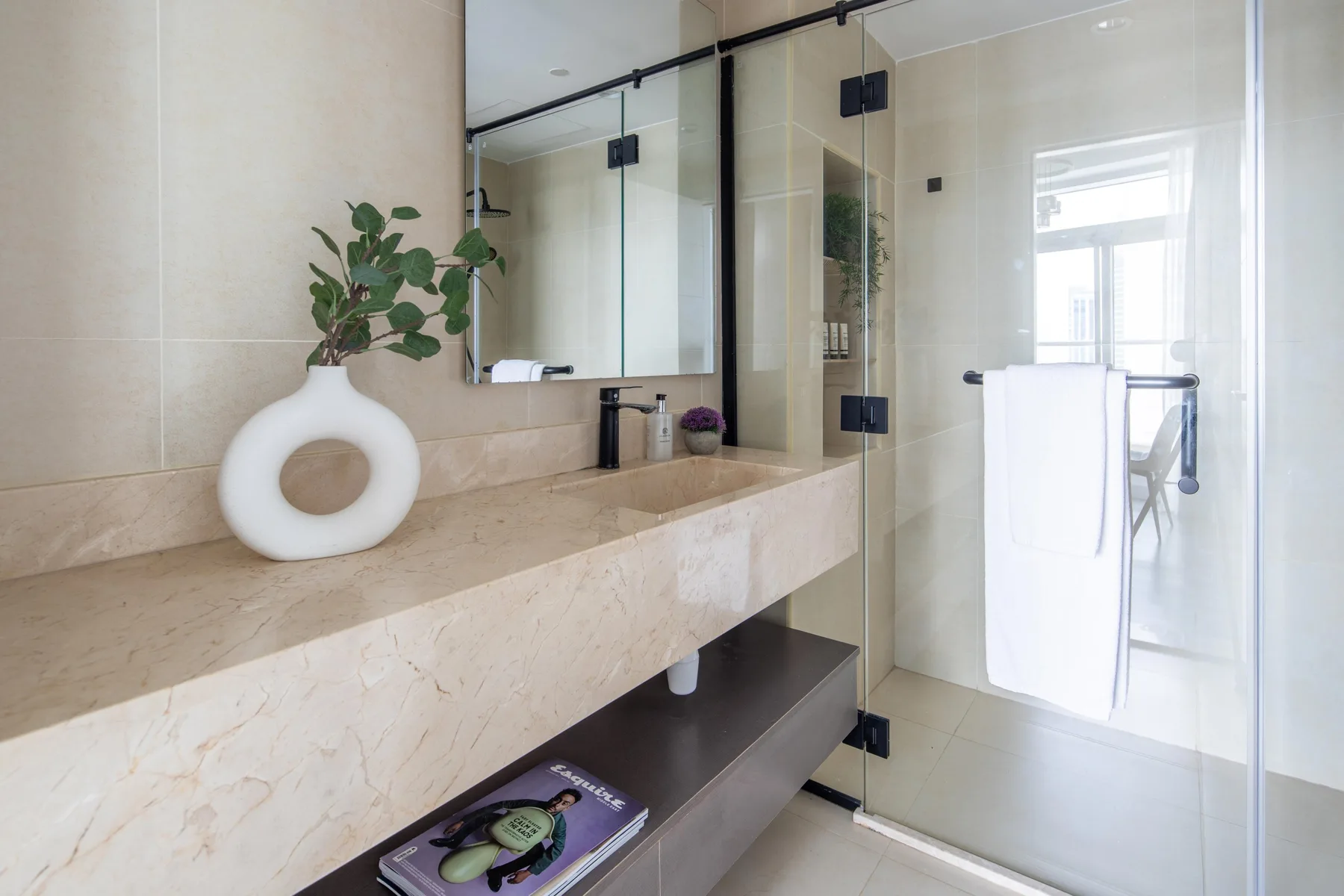 Un tocador de baño luminoso con espejo y ducha de vidrio.