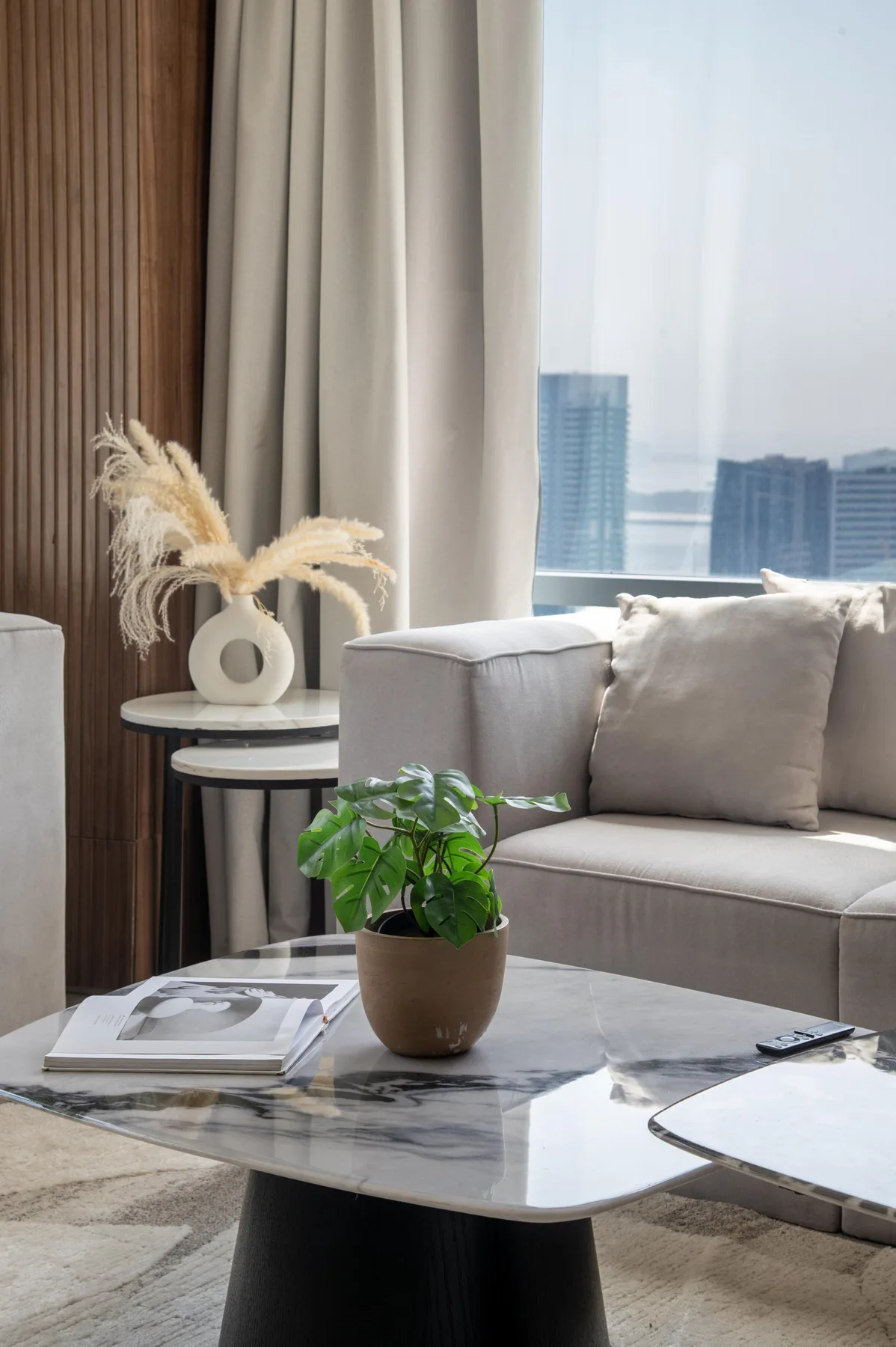 Una sala luminosa con asientos claros, una mesa de centro y vistas de la ciudad por la ventana.