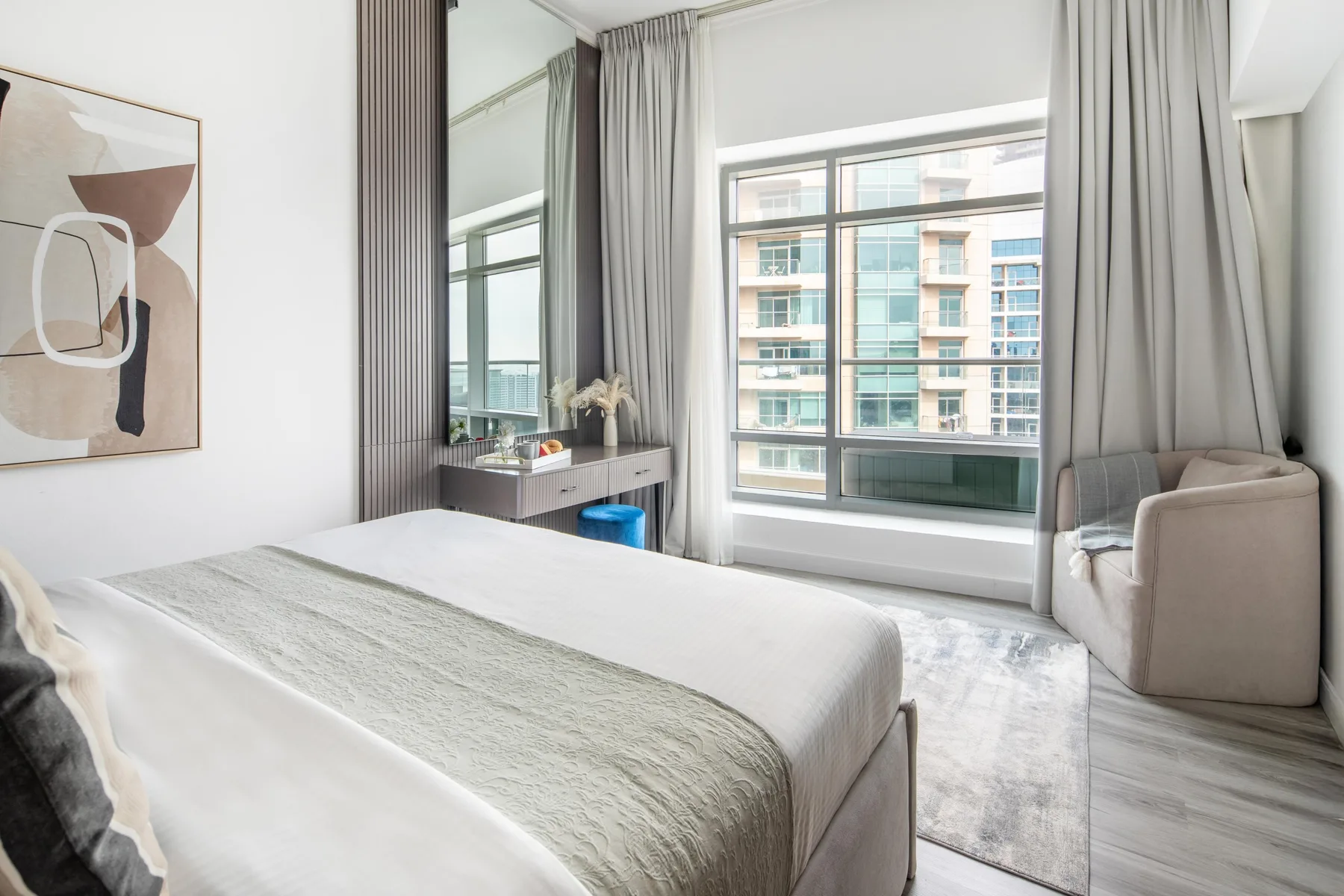 Un dormitorio luminoso con una cama grande, ventanales altos y una zona de estar.