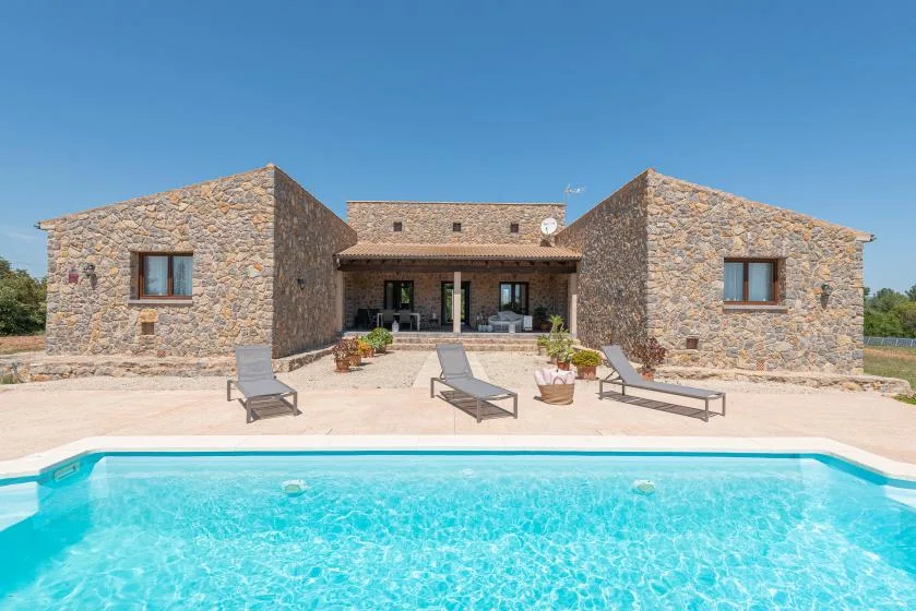 A stone house faces a swimming pool, with lounge chairs on the patio.
