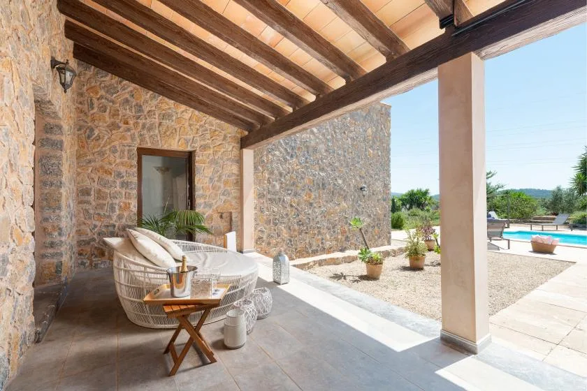 A covered stone patio with seating overlooks a swimming pool.