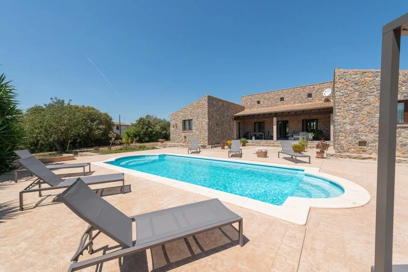 A swimming pool and patio seating sit in front of a stone-clad building.
