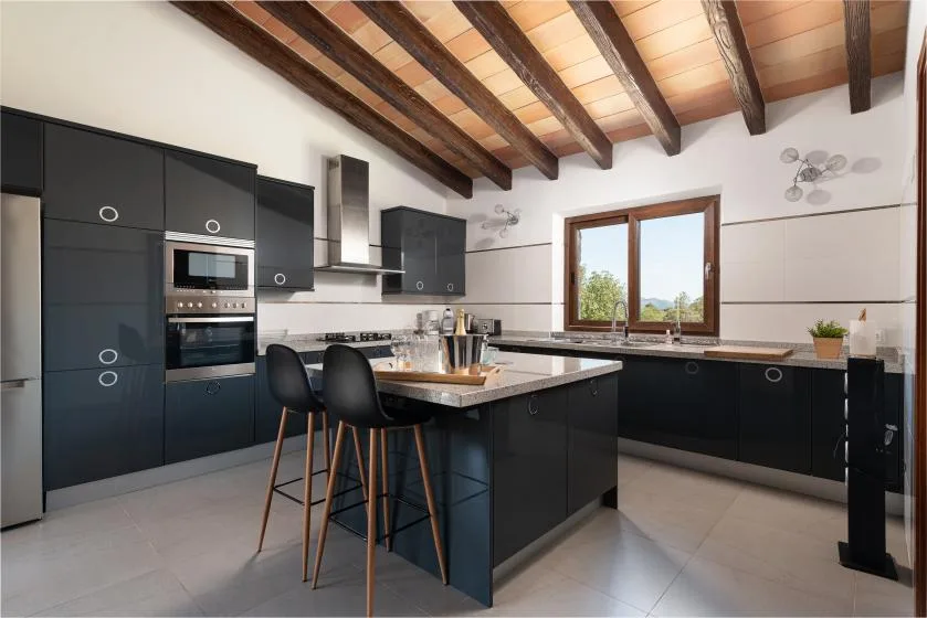 A modern kitchen with dark cabinetry, an island, and exposed ceiling beams.