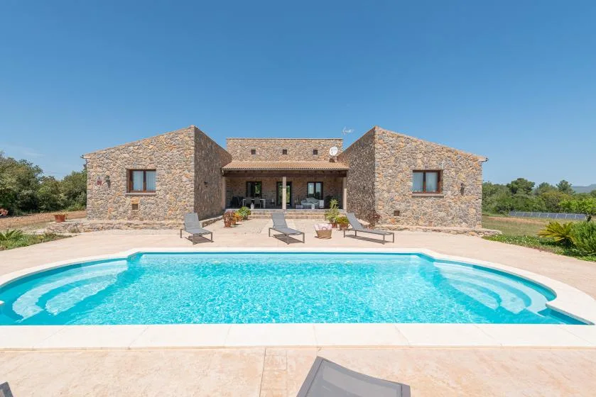 A stone-clad house stands behind a bright blue swimming pool.