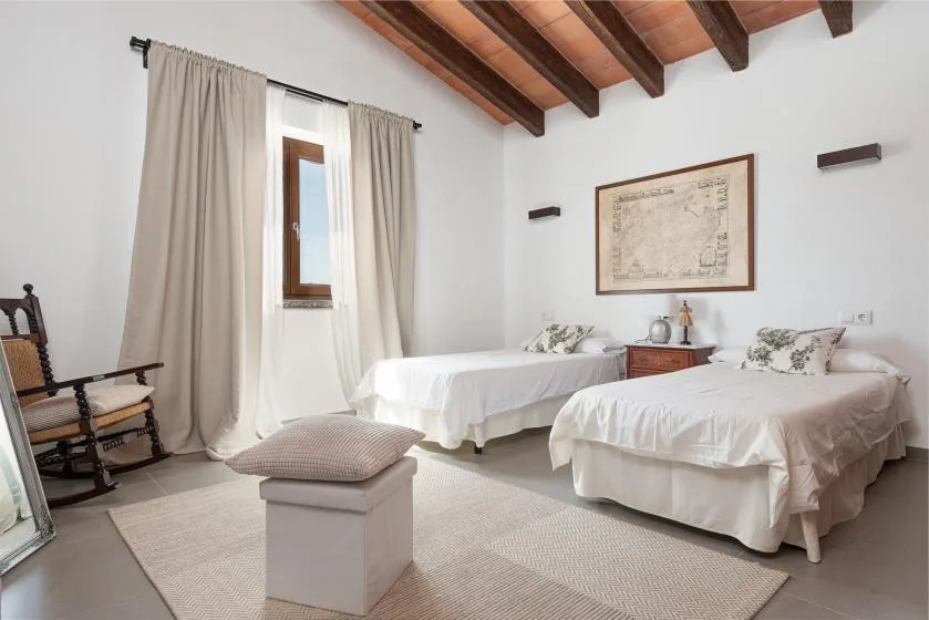 A bedroom with two beds, light curtains, and exposed ceiling beams.
