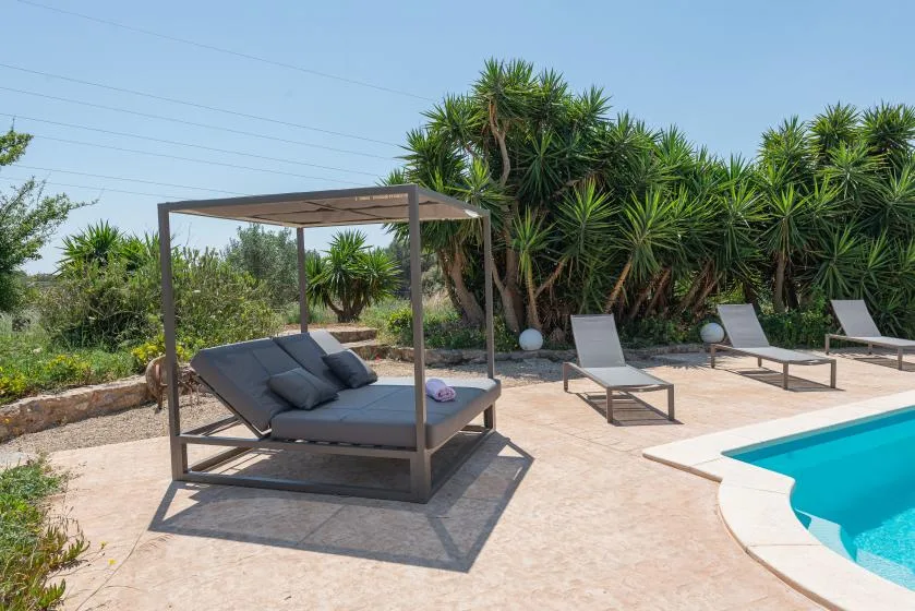 A poolside patio with shaded outdoor seating and loungers beside the water.