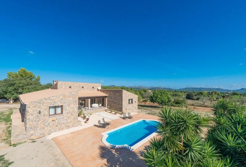 A stone house overlooks a bright blue swimming pool and surrounding countryside.