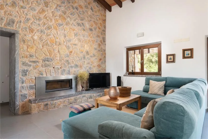 A living room with teal seating, a stone fireplace, and a wooden coffee table.