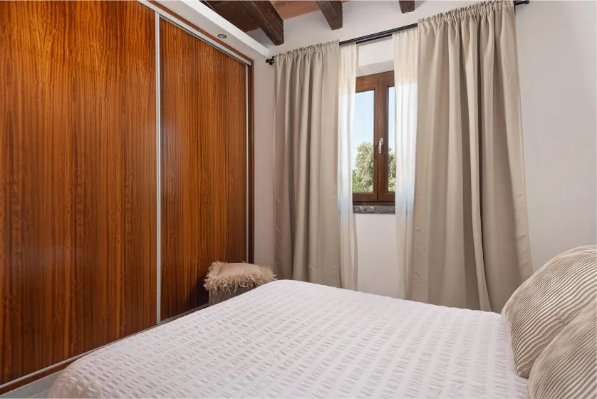 A bedroom with a bed, wooden wardrobe, and curtained window.