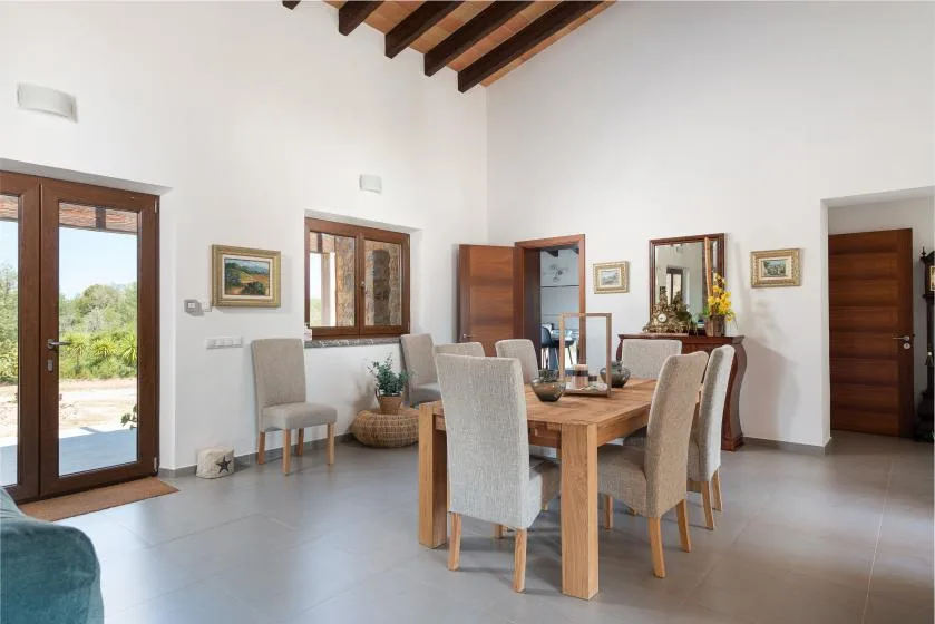 A dining area with a wooden table and upholstered seating beneath exposed ceiling beams.