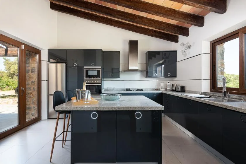 A modern kitchen with dark cabinetry, a central island, and exposed ceiling beams.