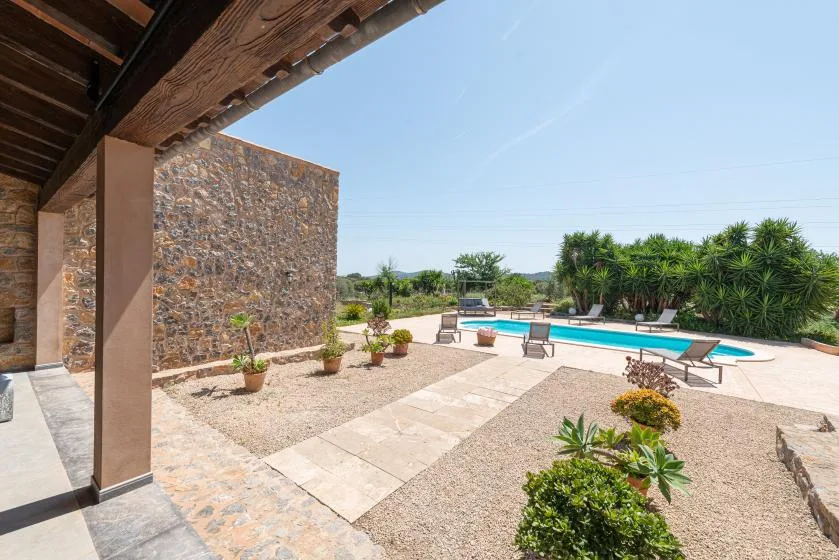 A stone patio overlooks a swimming pool and landscaped garden under a clear sky.