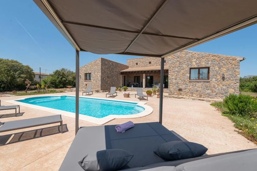 A swimming pool and stone house sit beside a shaded outdoor seating area.