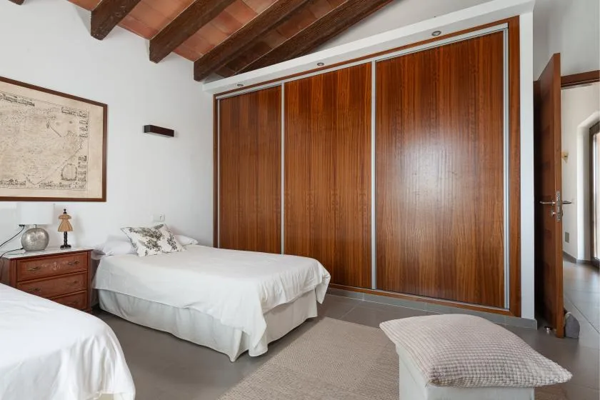 A bedroom with two beds, wood-paneled wardrobes, and exposed ceiling beams.