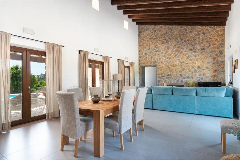 A bright living and dining area has a wooden table beside blue seating and tall windows.