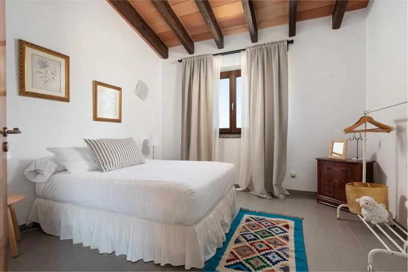 A bedroom with a neatly made bed beneath exposed wooden ceiling beams.