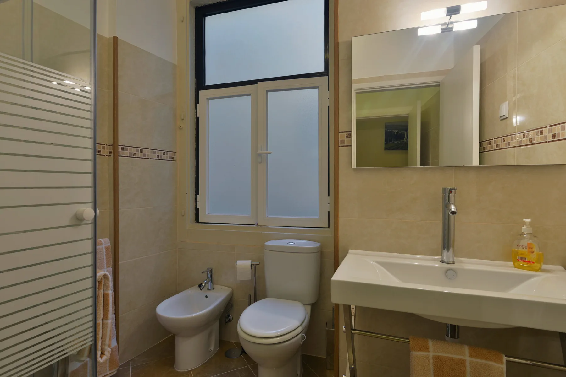 Un baño con lavabo, inodoro, bidé y mampara de ducha de vidrio.