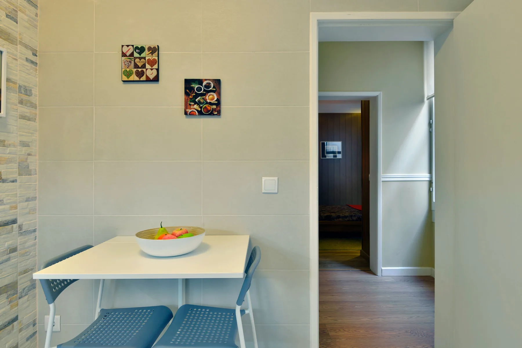 Una zona de comedor alicatada con una mesa pequeña y asientos junto a una puerta abierta.
