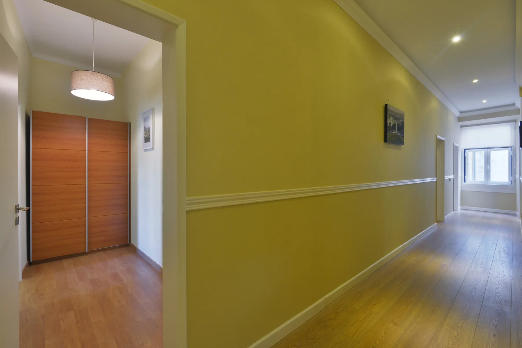 Un pasillo interior con paredes amarillas, suelo de madera y una puerta.