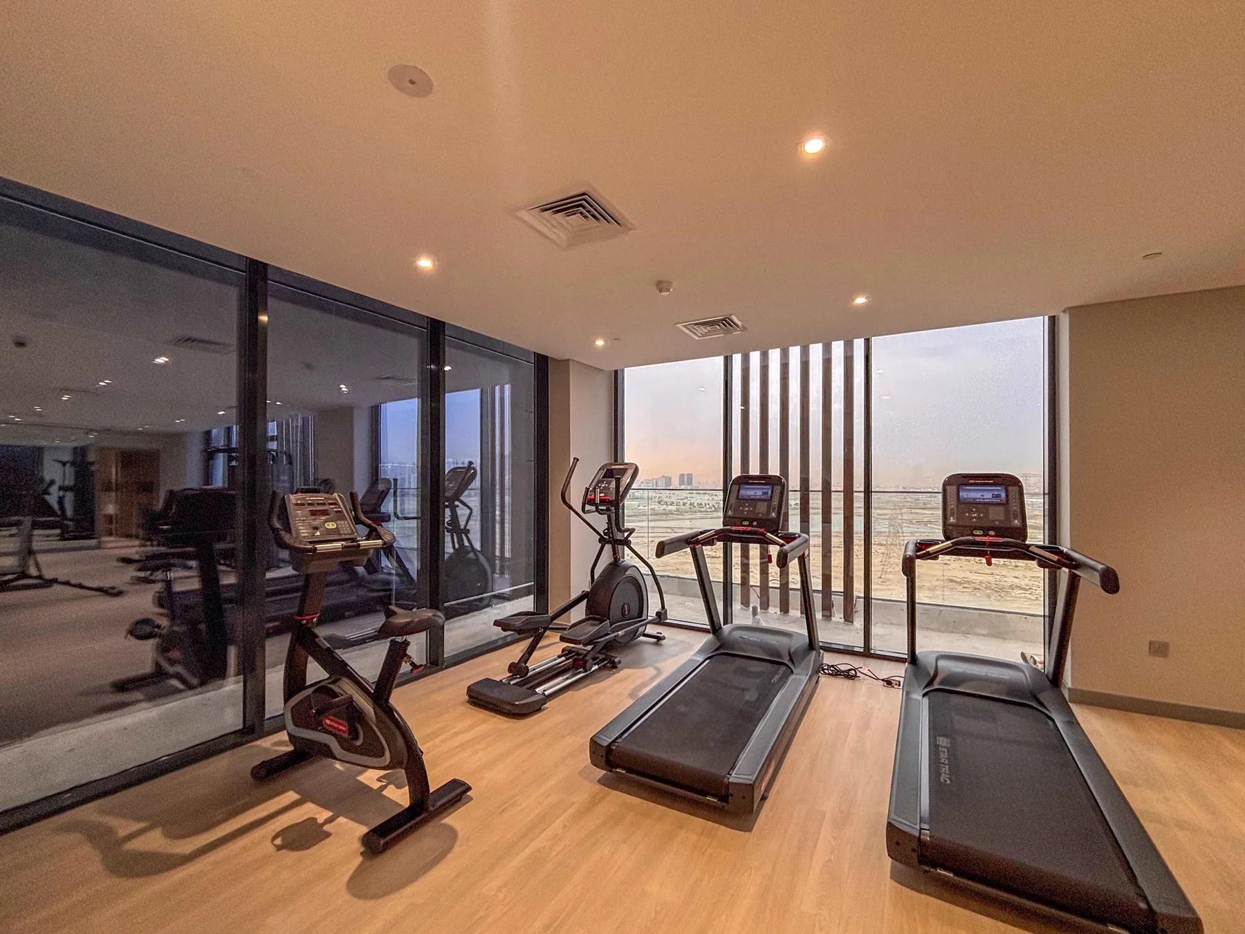 Un gimnasio luminoso con cintas de correr y bicicletas estáticas junto a grandes ventanales.