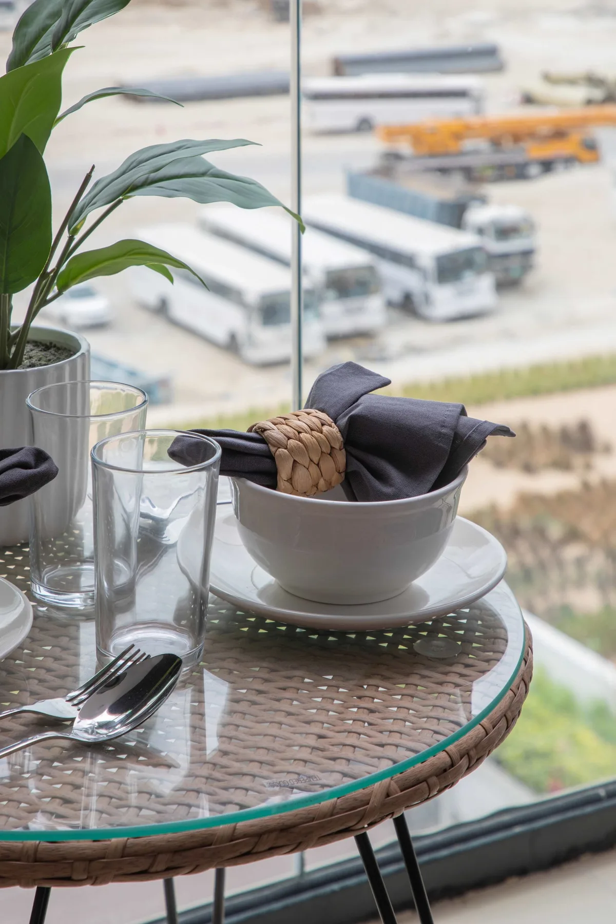 Una mesa de patio con cubierta de vidrio sostiene vasos y un cuenco con servilletas dobladas.