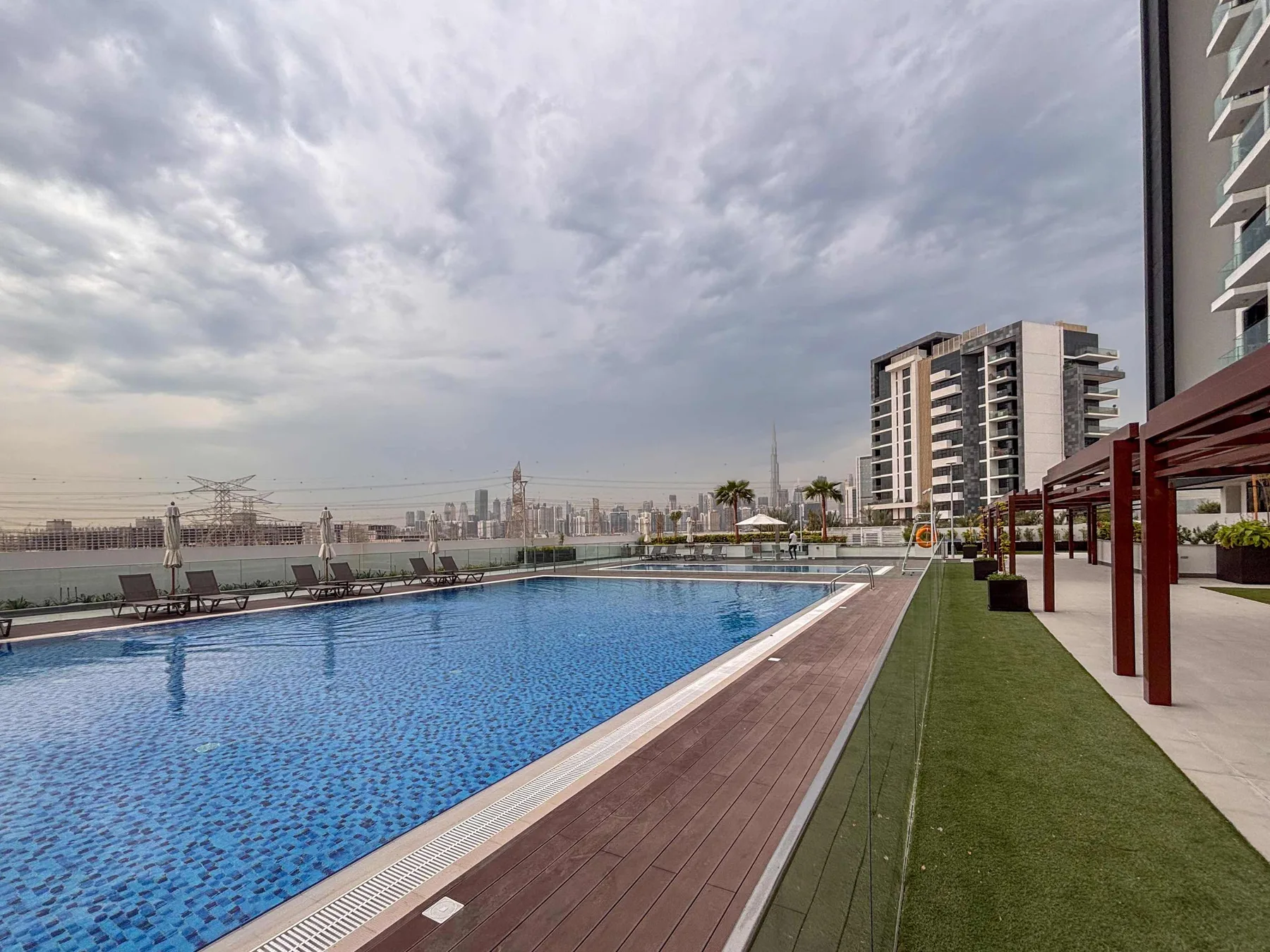 Una piscina al aire libre junto a una terraza y una zona ajardinada con asientos.