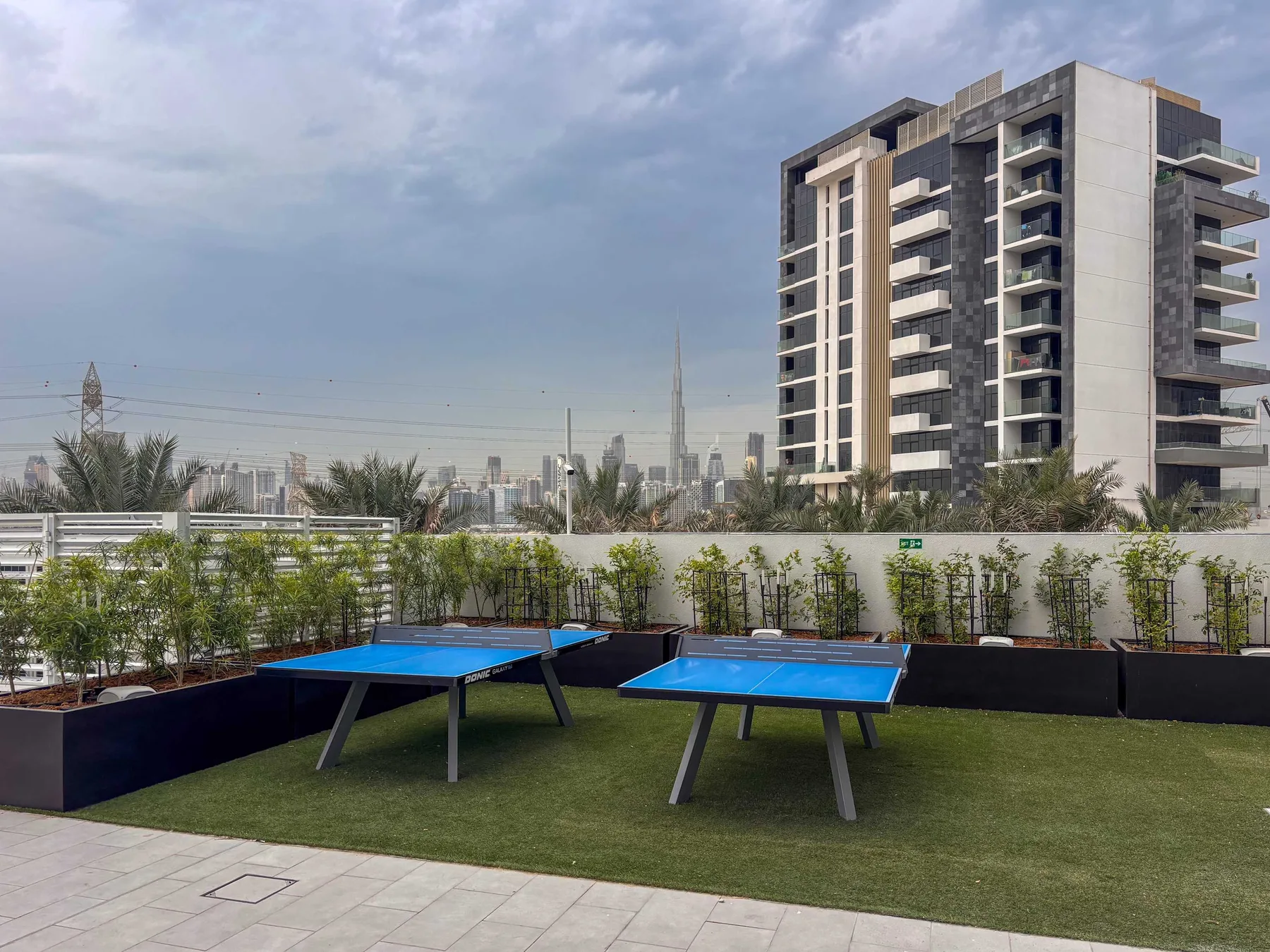 Una zona recreativa en la azotea tiene dos mesas de ping-pong azules junto al horizonte urbano.