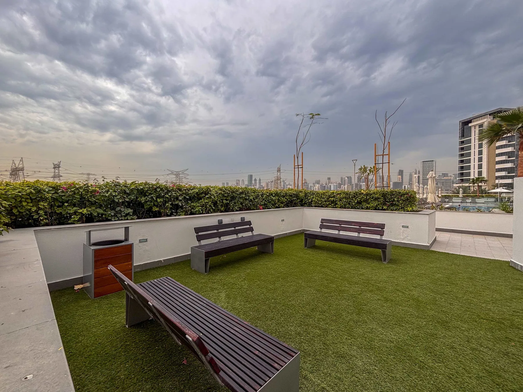 Una terraza en la azotea tiene varios bancos sobre césped artificial, con edificios de la ciudad a lo lejos.