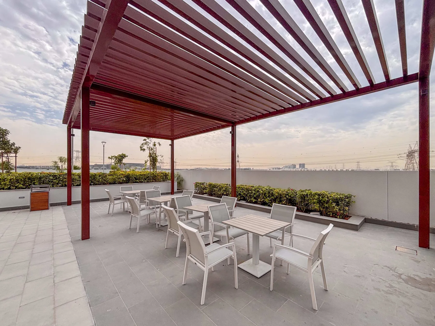 Un patio exterior con mesas y asientos bajo una pérgola de listones.