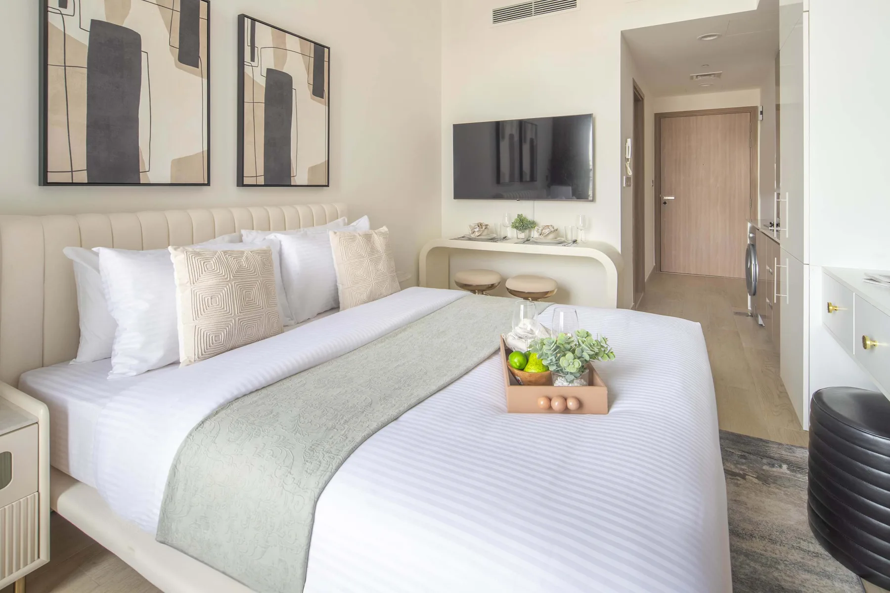 Un dormitorio luminoso con una cama bien tendida y un televisor en la pared.