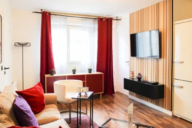 A living room with seating, red curtains, and a wall-mounted television.