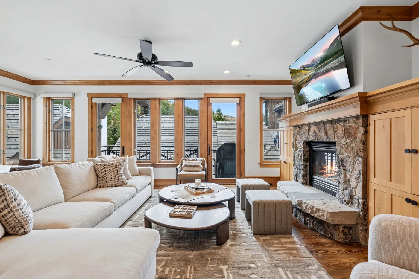 A living room with light seating, a stone fireplace, and large windows.