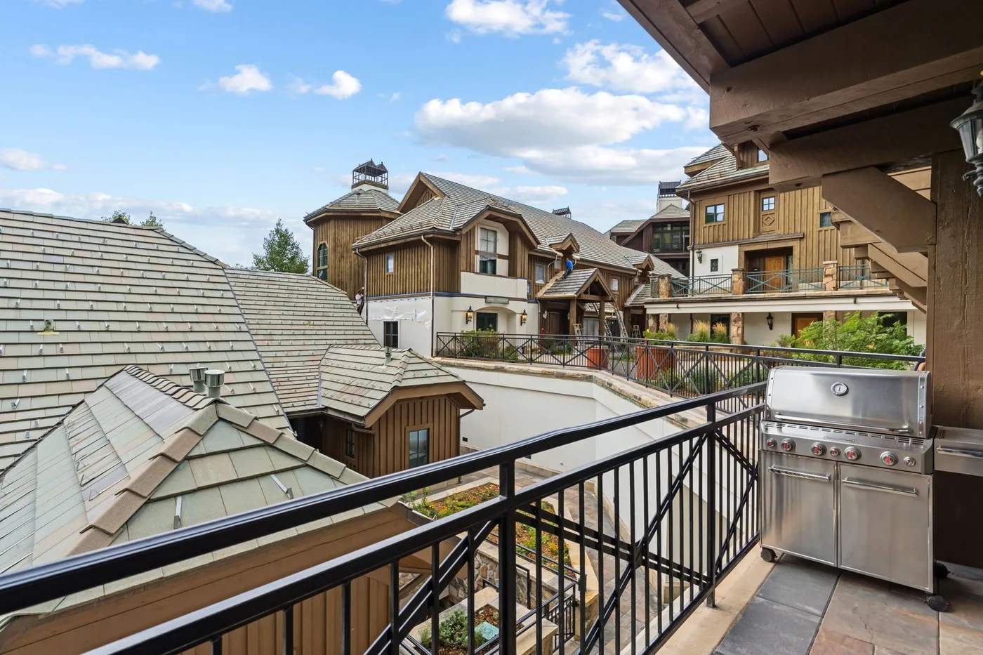 A balcony overlooks neighboring chalet-style buildings and rooftops beneath a partly cloudy sky.