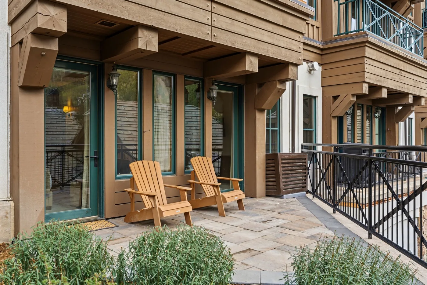 A patio with wooden seating beside glass doors and a black metal railing.
