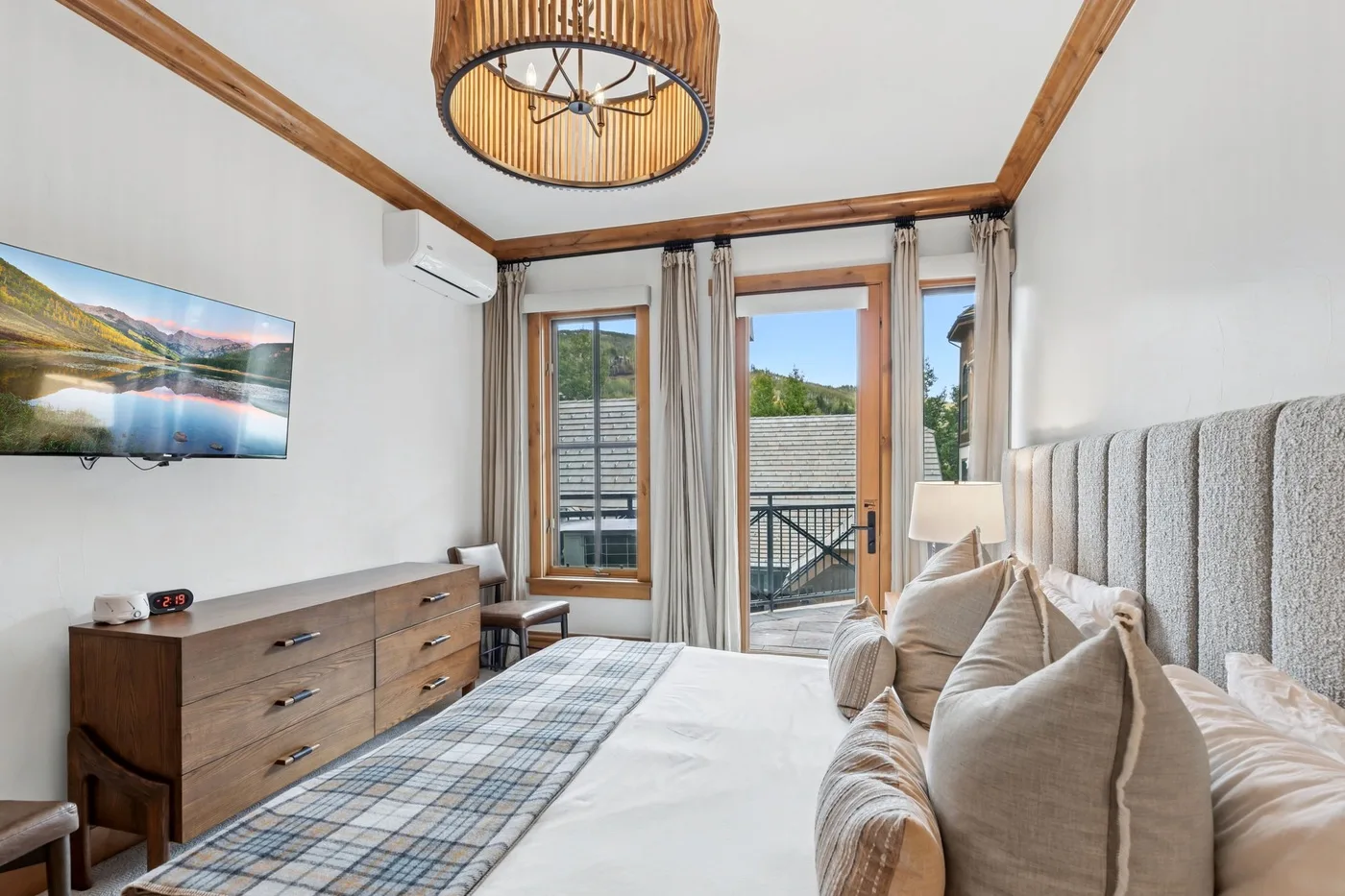 A bedroom with a bed, wooden dresser, and windows opening onto a balcony.