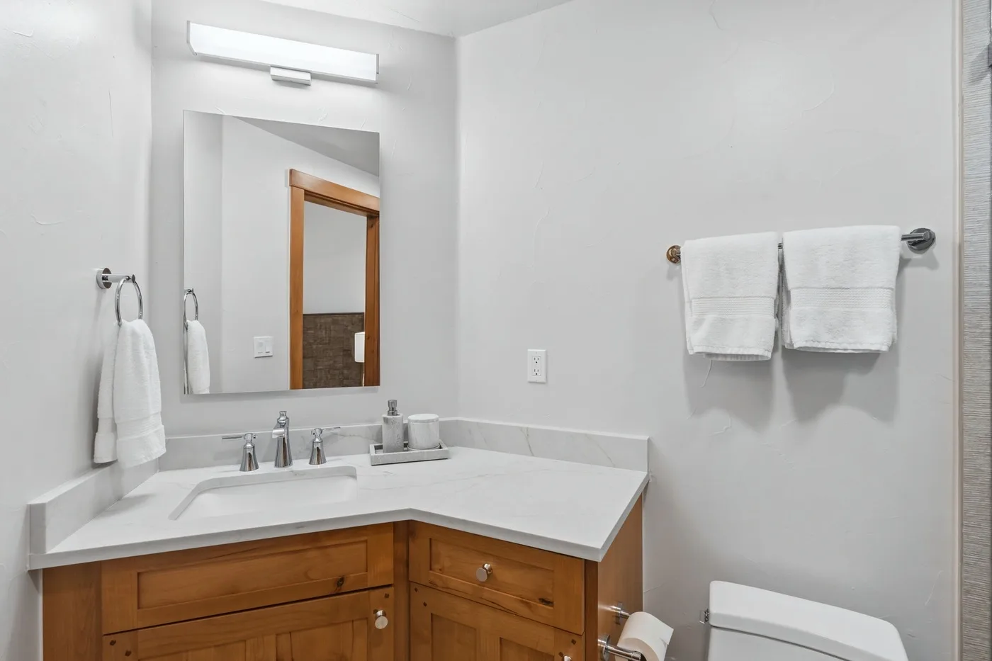 A bright bathroom with a corner vanity, mirror, and towels.