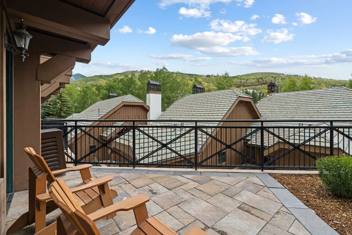 A paved terrace with wooden seating overlooks nearby rooftops and green hills.