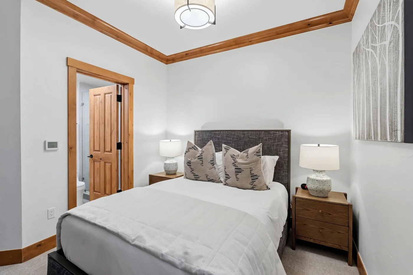 Bedroom with a neatly made bed, bedside tables, and a wooden-trimmed doorway.