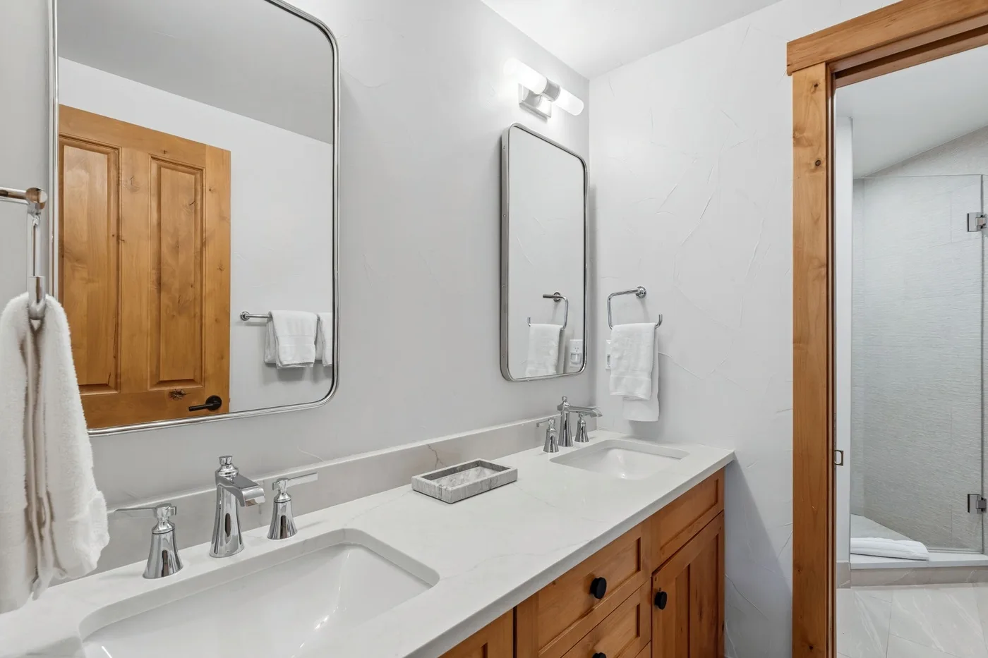 A bathroom vanity with two sinks and a mirror beside a shower.