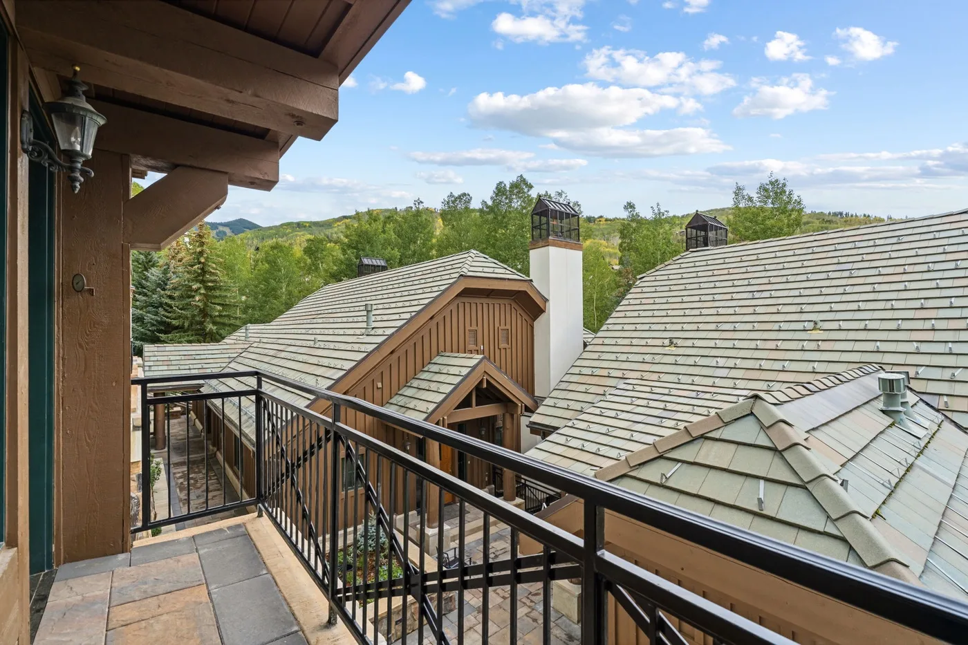 A balcony overlooks several pitched rooftops and a green, tree-lined landscape.