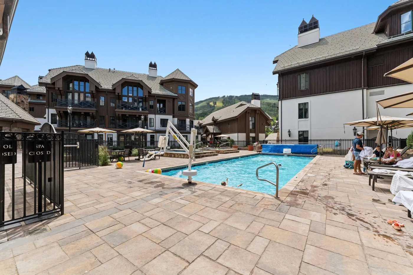 An outdoor swimming pool sits among multi-story buildings on a sunny day.