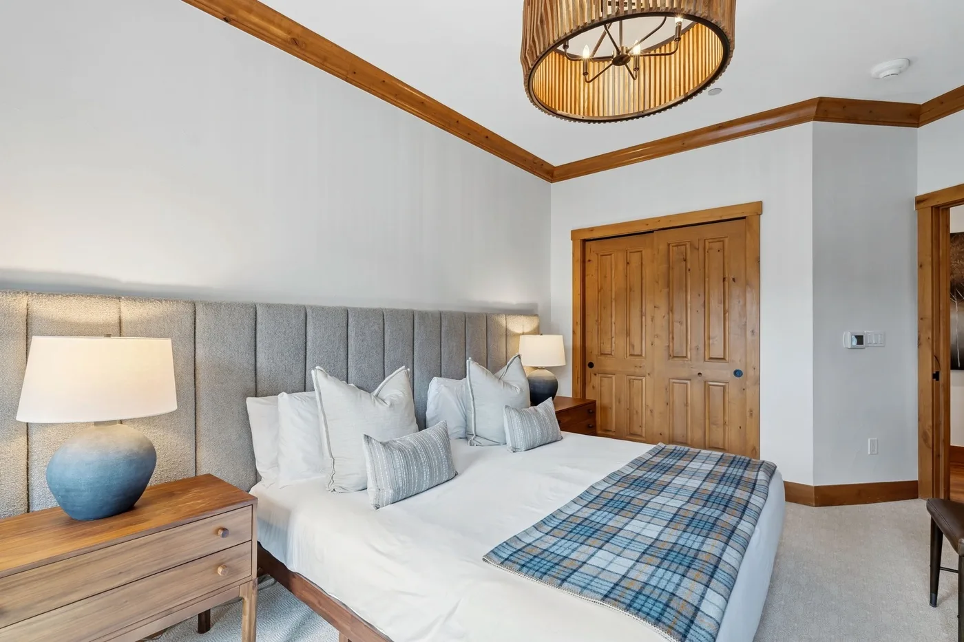 A bedroom with a bed, gray upholstered headboard, and wooden double doors.
