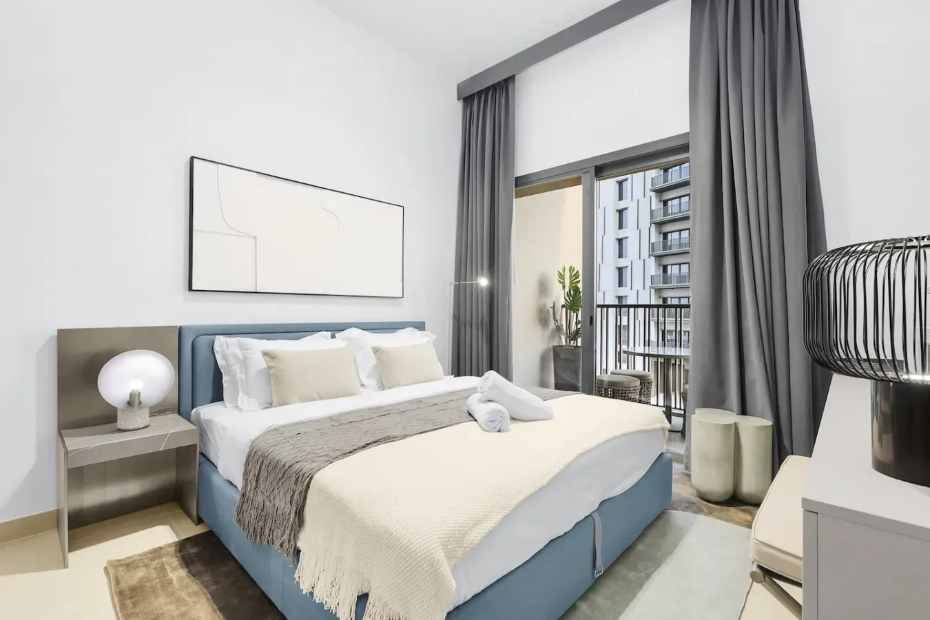 A bedroom with a large bed, bedside tables, and curtains beside a balcony window.