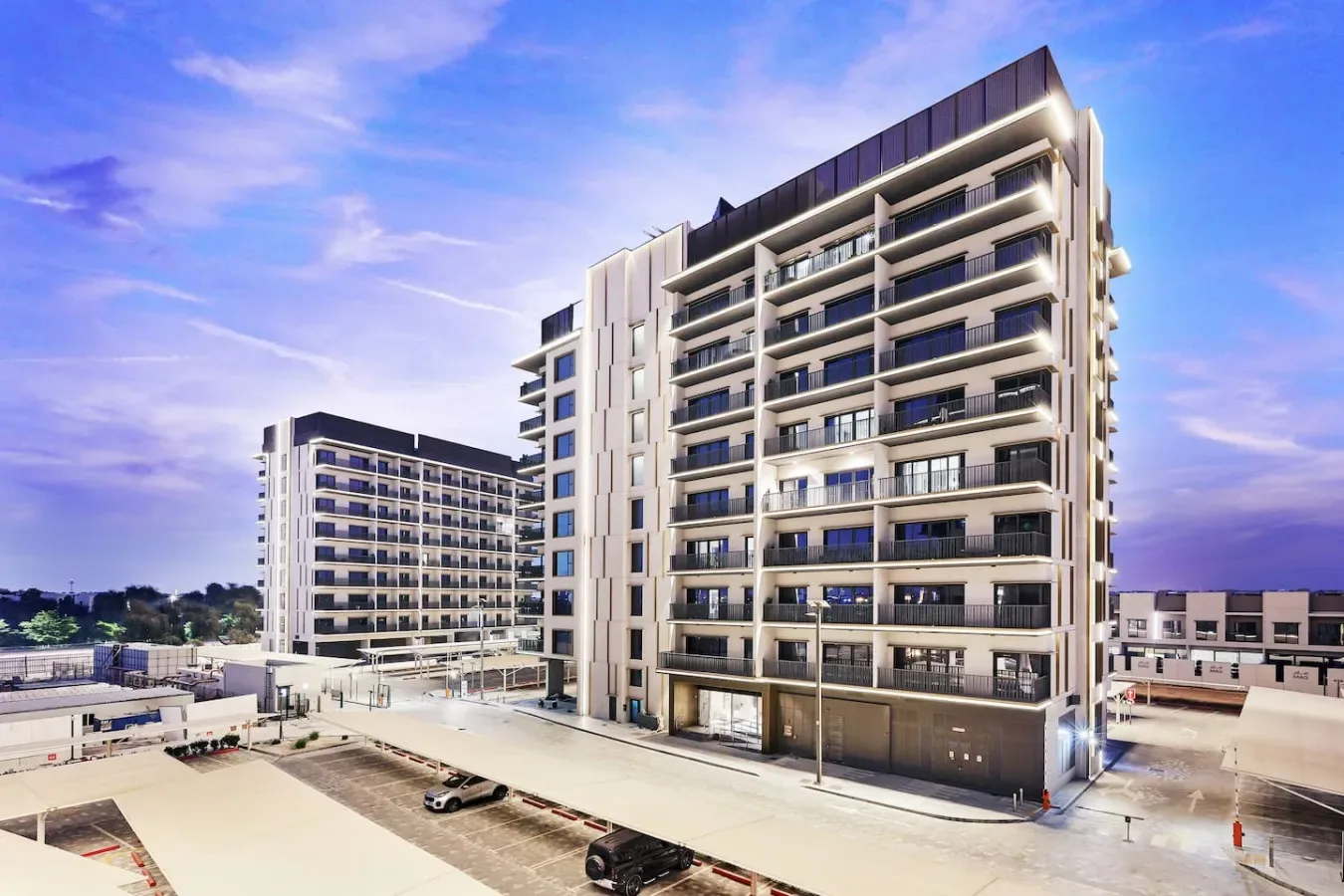 Modern multi-story buildings with balconies stand beside a paved parking area.