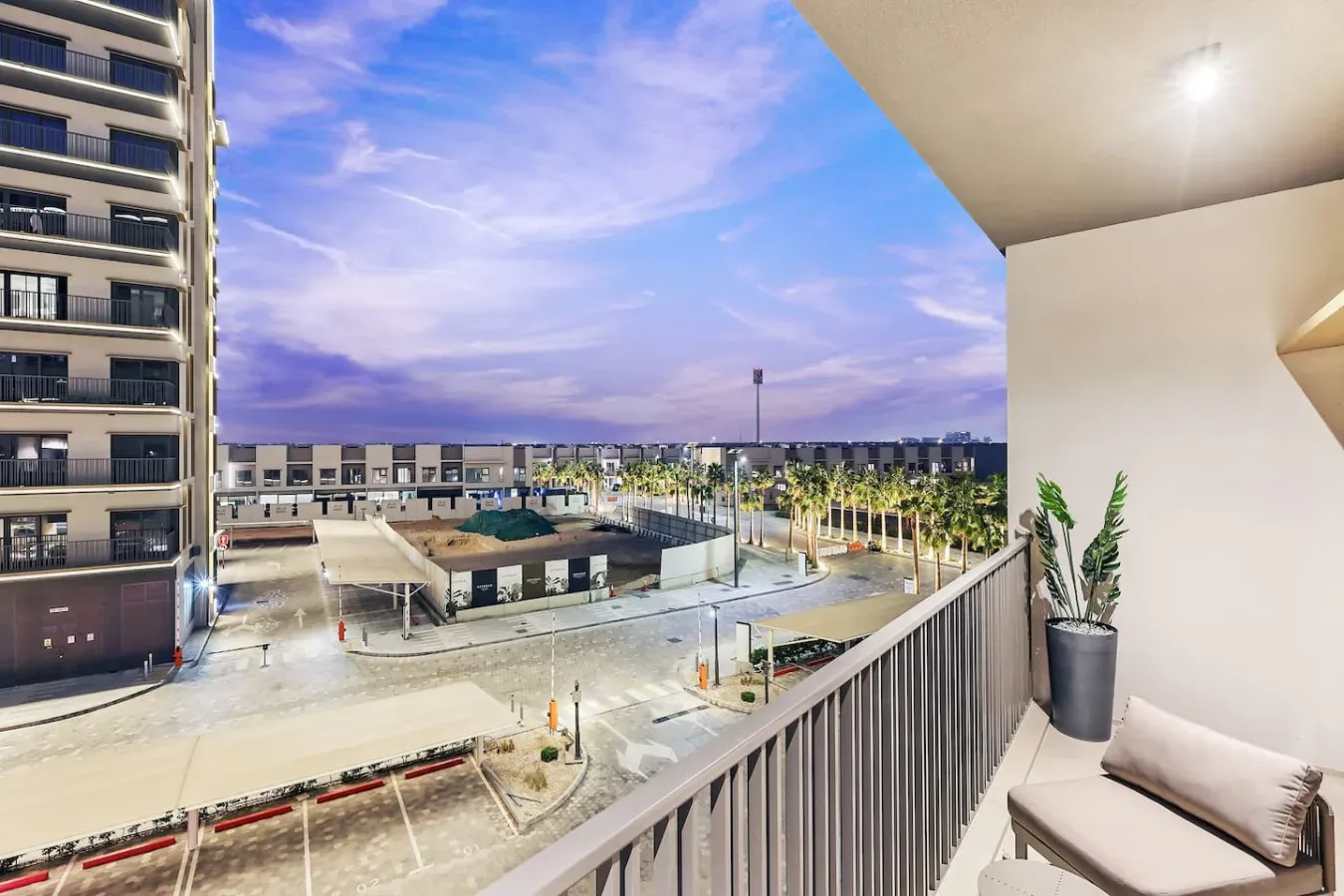 Un balcón da a un complejo residencial con un patio ajardinado al atardecer.
