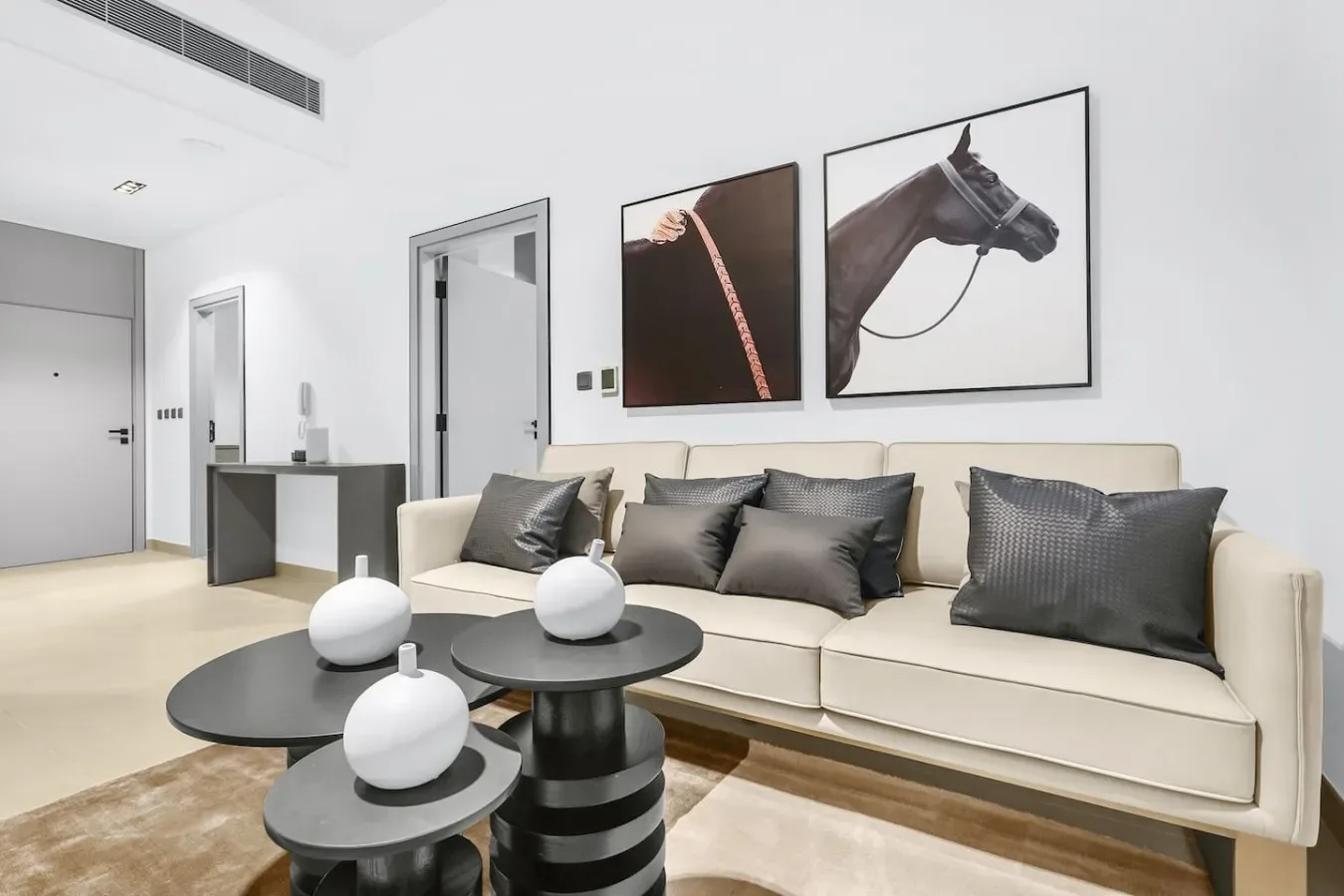 A bright living room with a long beige sofa and two framed horse photographs.