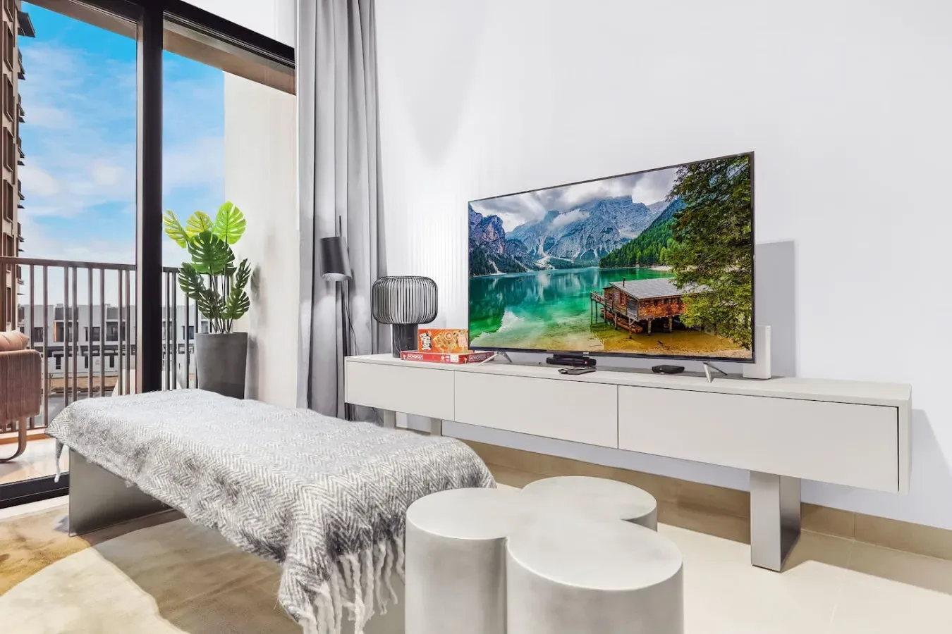 Una sala luminosa con televisor, mueble bajo y puertas al balcón.
