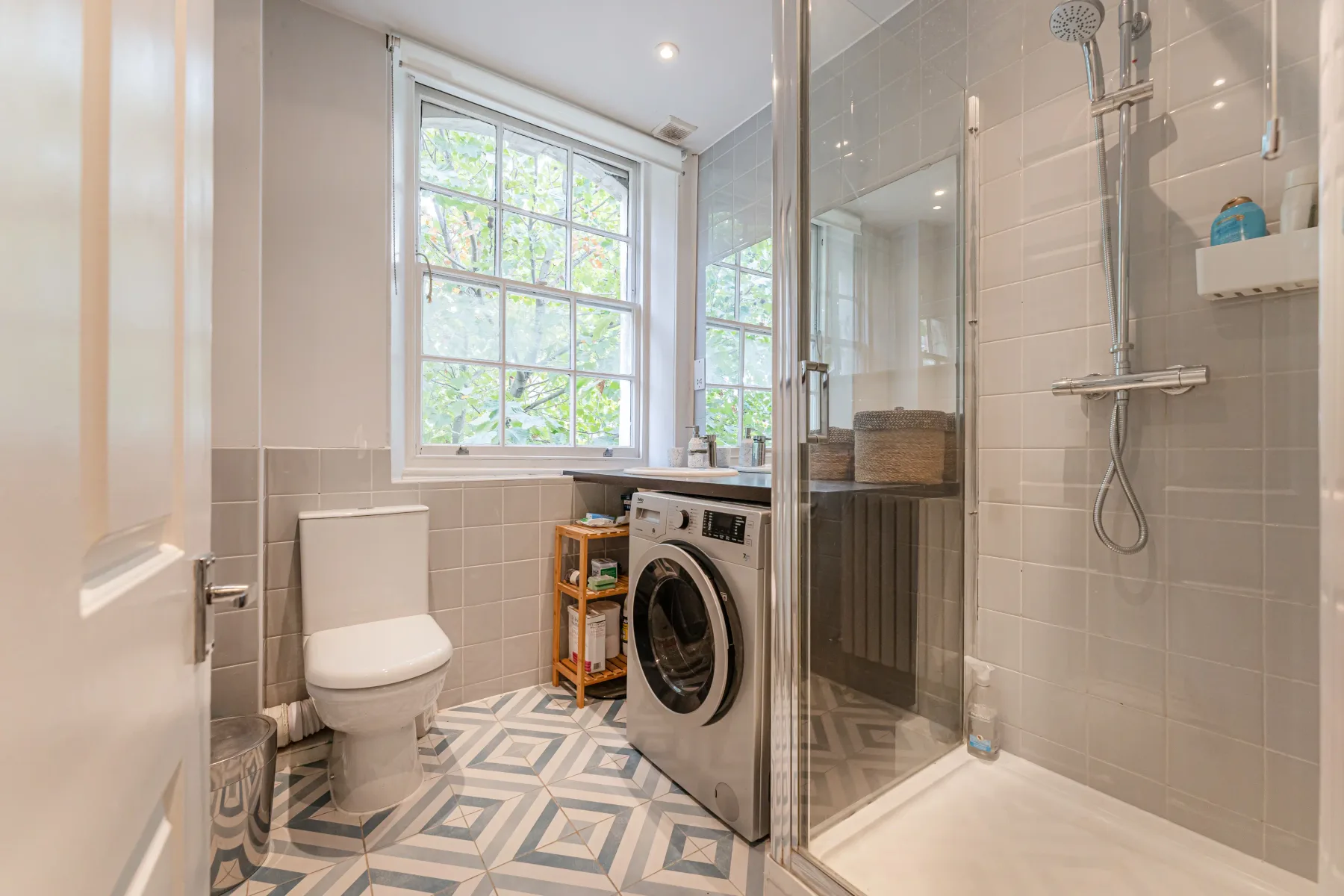 Un baño con ducha, inodoro y lavadora junto a una ventana.