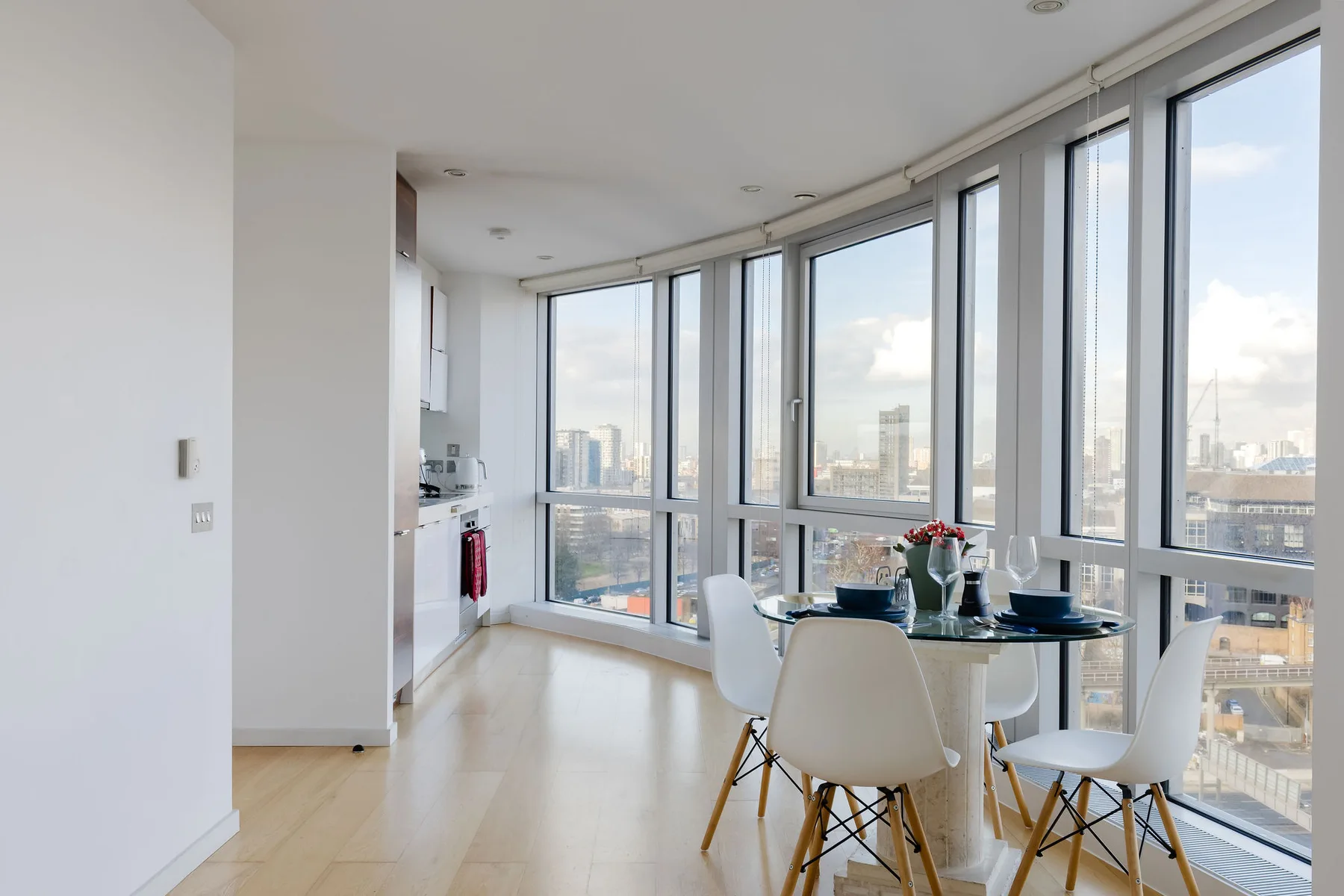 A bright dining area with a table and seating beside floor-to-ceiling windows.