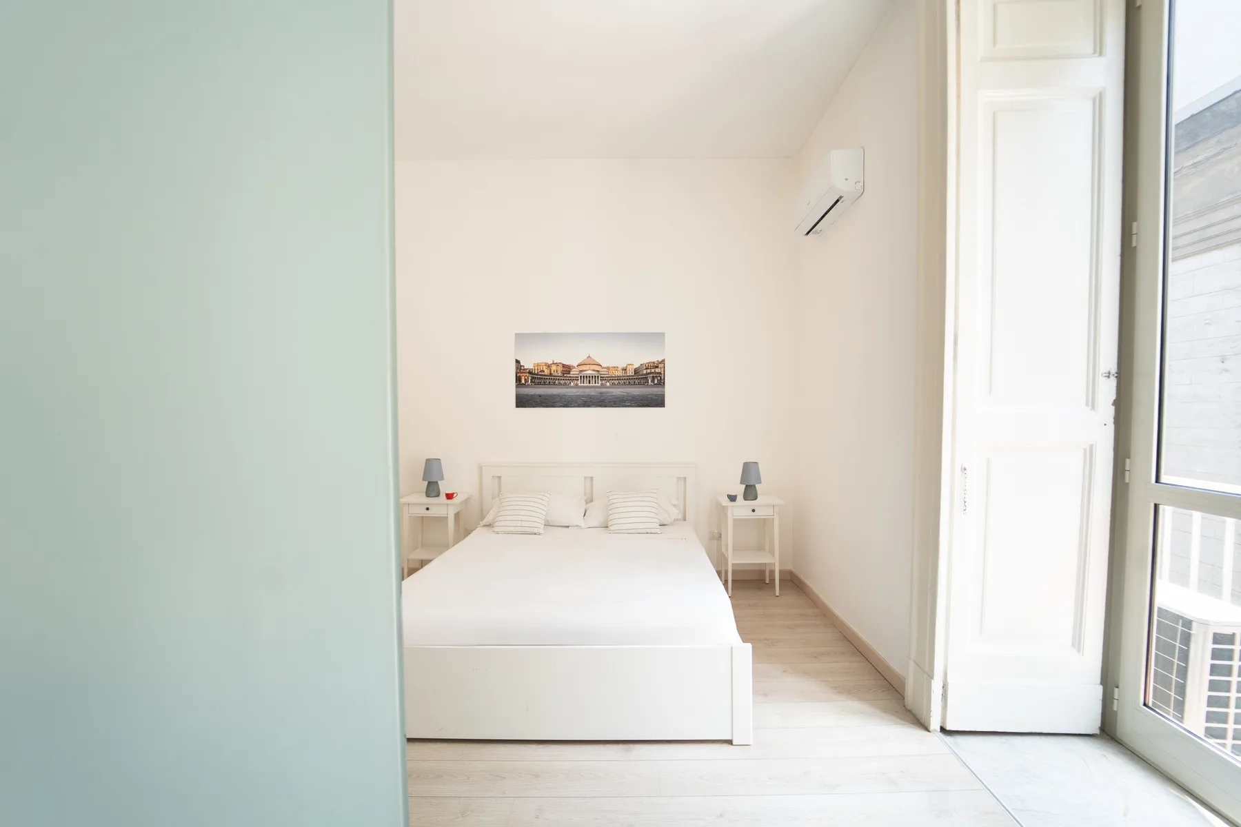Un dormitorio luminoso con una cama, mesitas de noche y una ventana grande.